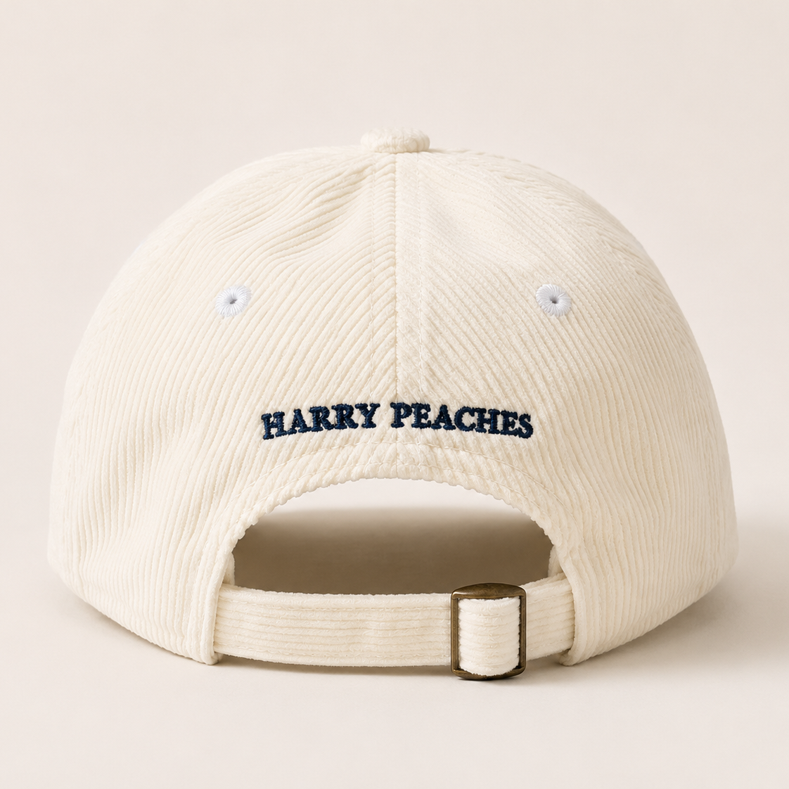An off-white corduroy baseball cap shown from the back, featuring the text 'HARRY PEACHES' embroidered in navy blue on the back panel and an adjustable strap with a metal buckle.