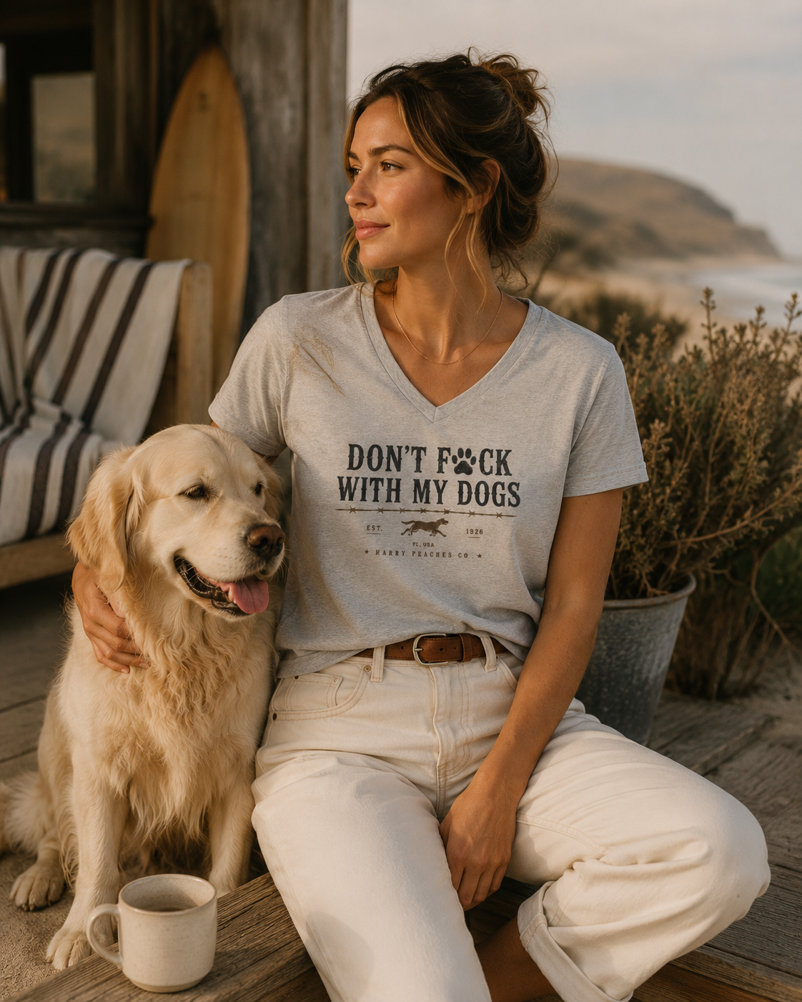 Woman sitting with a dog wearing a t-shirt with text, outdoors by a body of water.