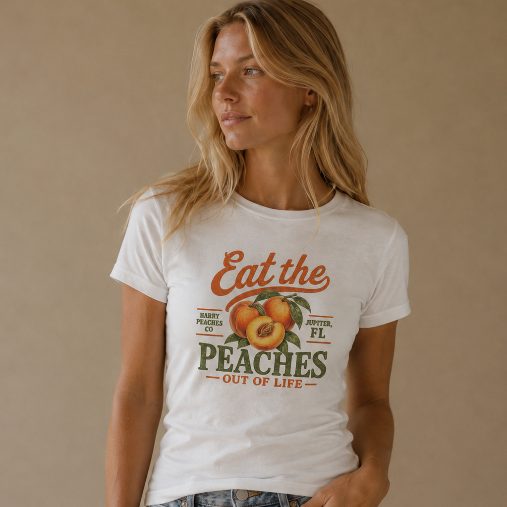 A woman wearing a white graphic t-shirt with a retro peach design and light-wash blue jeans, standing against a solid beige background.
