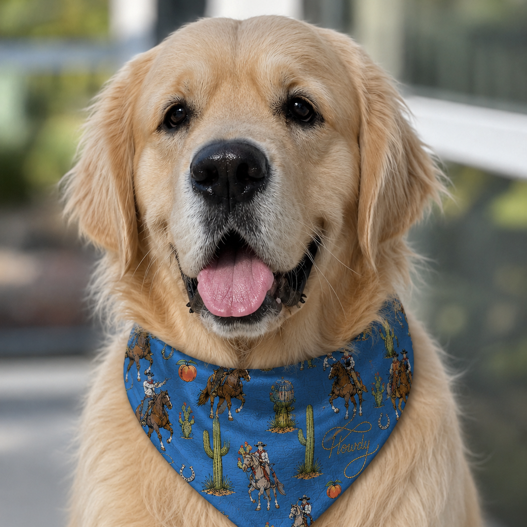 A golden retriever dog wearing a blue bandana with a cowboy and cactus print, photographed outdoors with a blurred background.
