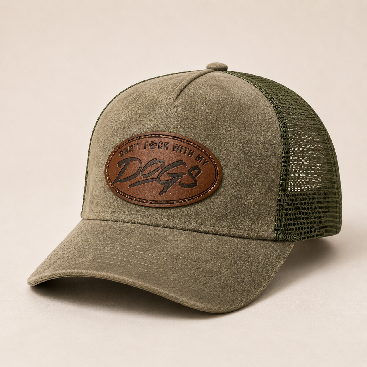 An olive green trucker hat with a brown leather patch on the front that reads 'DON'T F*CK WITH MY Dogs'. The front panel and brim are a textured olive green fabric, while the back mesh is a darker forest green.