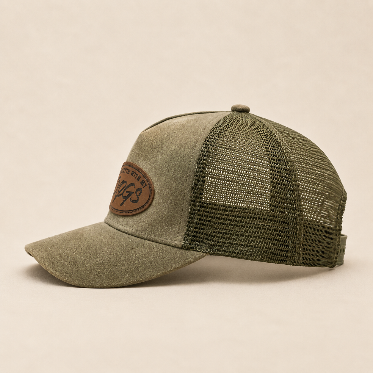 An olive green trucker cap with a textured fabric front panel, matching mesh back, and a brown leather patch on the side.