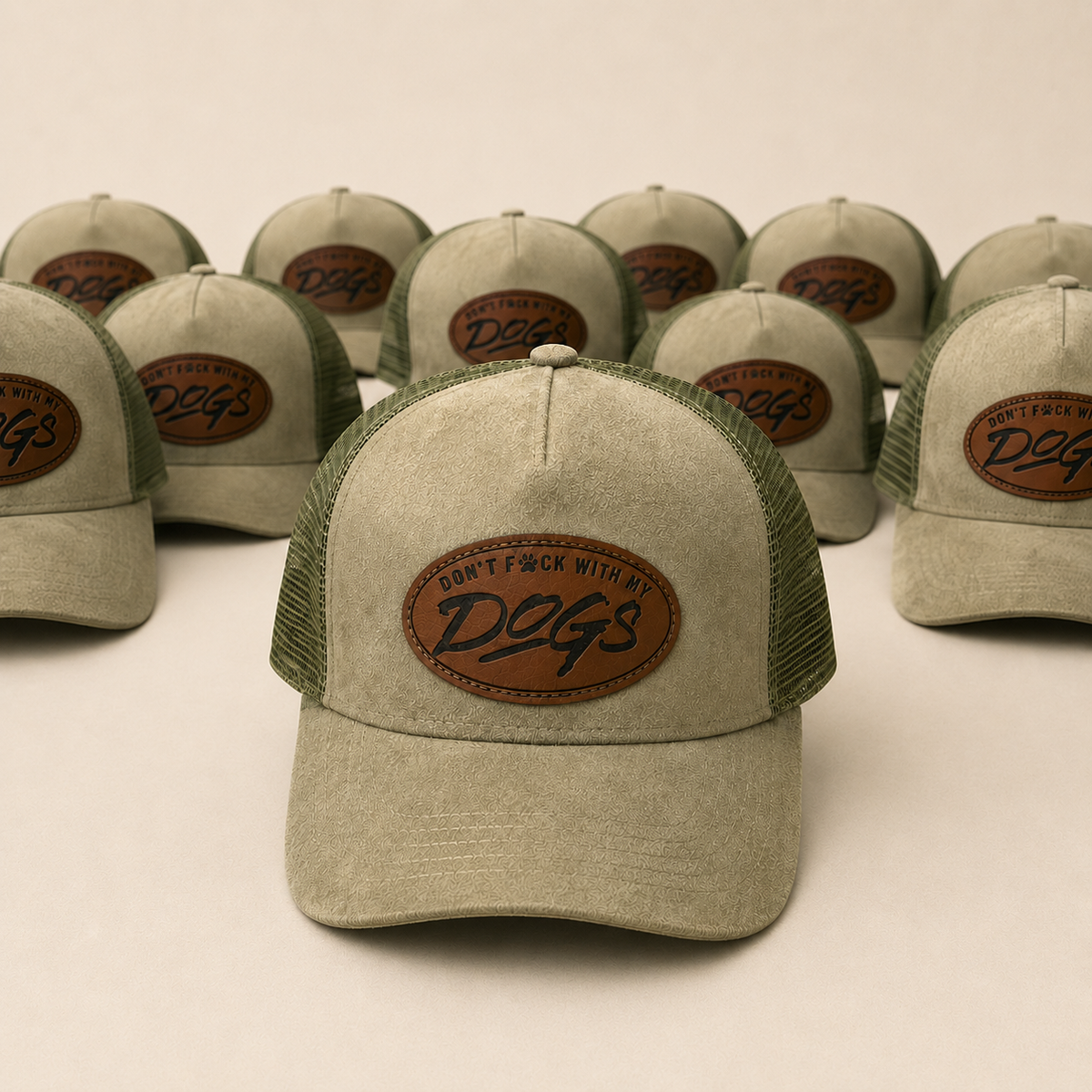 A group of trucker hats arranged in rows on a light beige studio background. The front hat is in sharp focus, showing a washed off-white canvas front panel and brim, olive green mesh back, and a brown oval patch with the text 'DON'T F*CK WITH DOGS'.