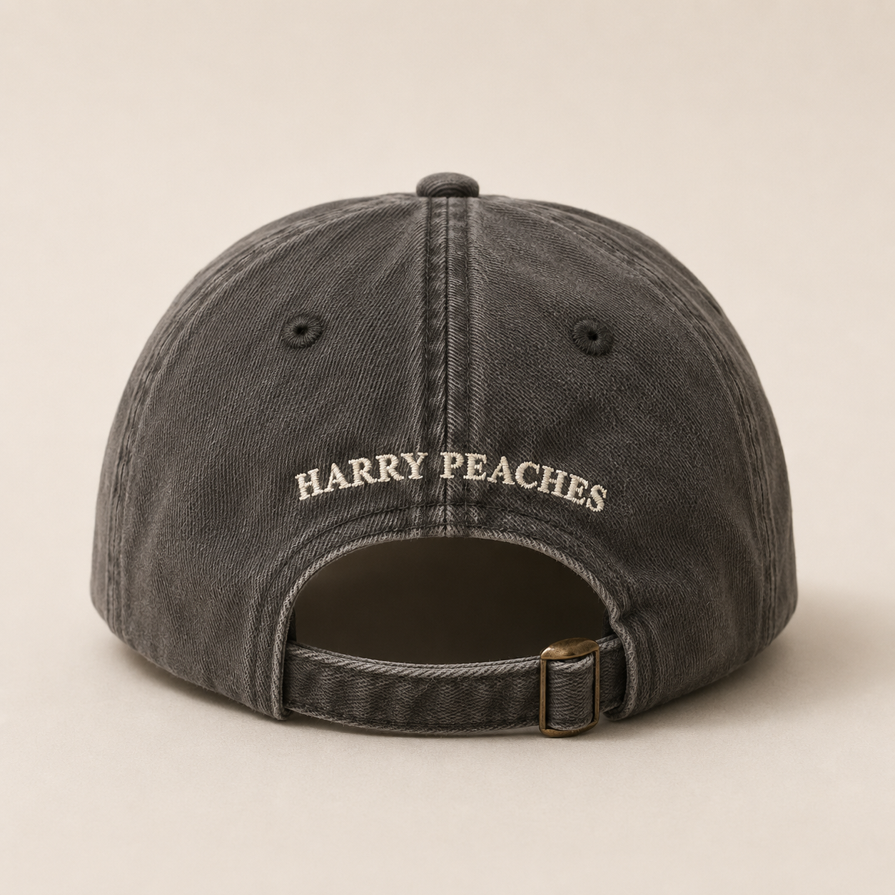 A dark gray washed cotton baseball cap shown from the back, featuring the embroidered text 'HARRY PEACHES' in cream on the crown and an adjustable strap with a brass-tone buckle.