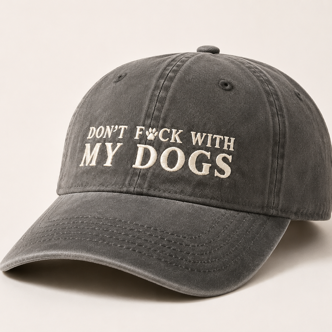A dark gray washed baseball cap with the phrase 'DON'T F*CK WITH MY DOGS' embroidered in white on the front, set against a plain light beige background.