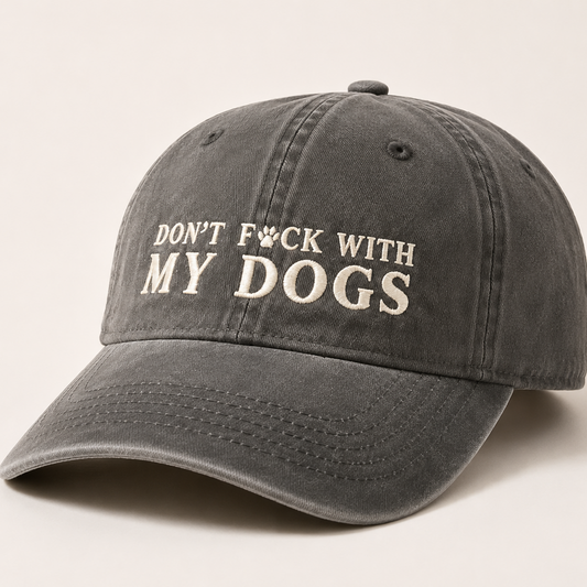 A dark gray washed baseball cap with the phrase 'DON'T F*CK WITH MY DOGS' embroidered in white on the front, set against a plain light beige background.