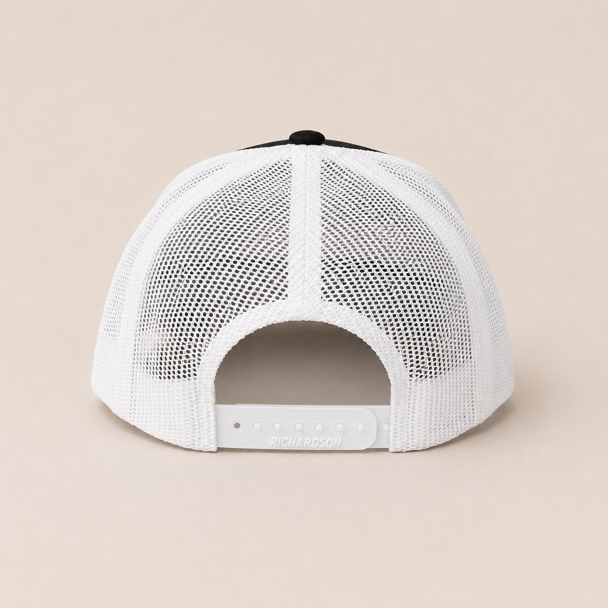 White trucker-style baseball cap shown from the back, featuring a white mesh back and a black button on top, photographed against a solid beige background.