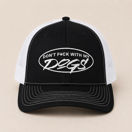 A black and white trucker hat with a black front panel and brim, white mesh back panels, and white embroidered text reading 'DON'T F*CK WITH MY DOGS' inside an oval on the front.
