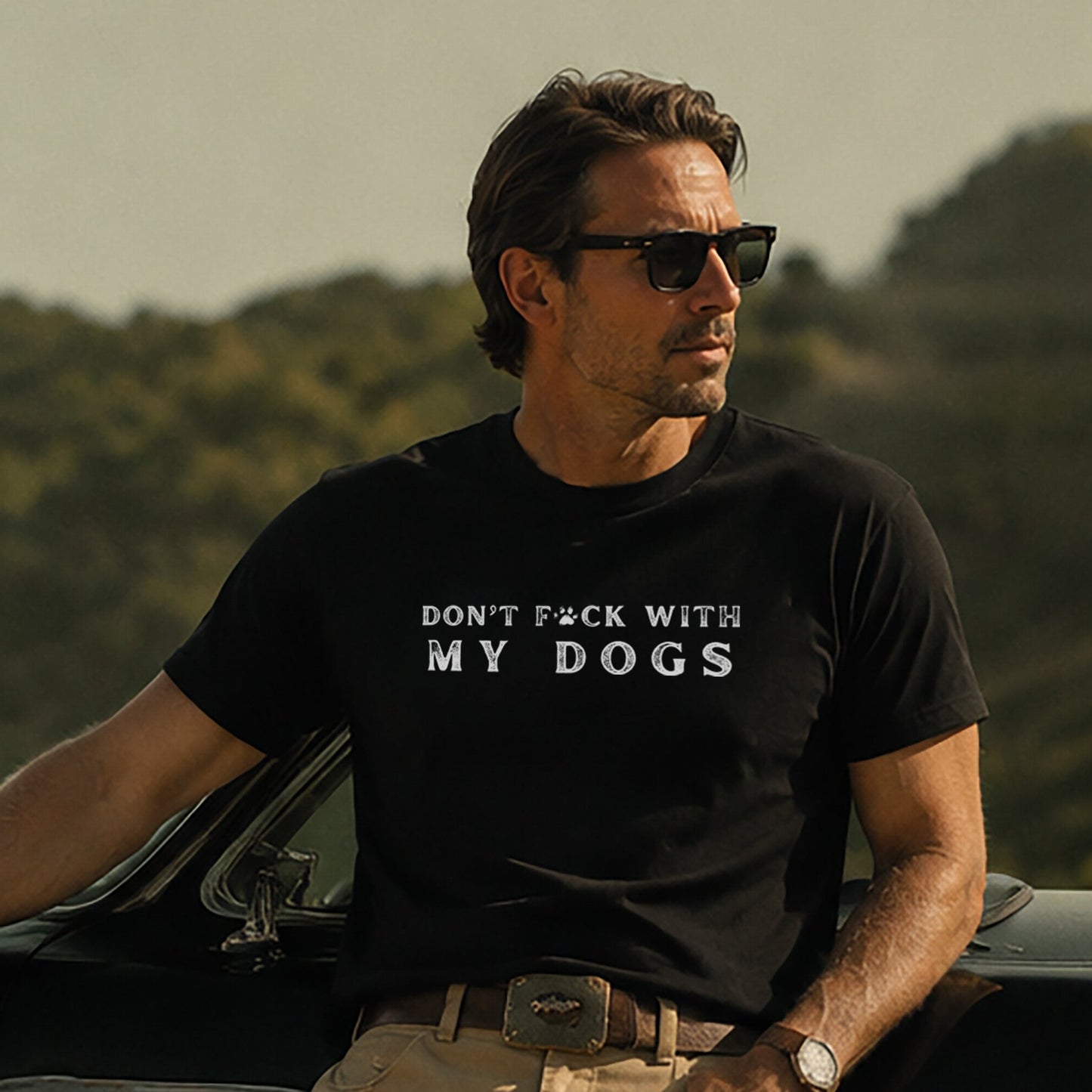 Man wearing a black t-shirt with text standing next to a dog by a car outdoors.