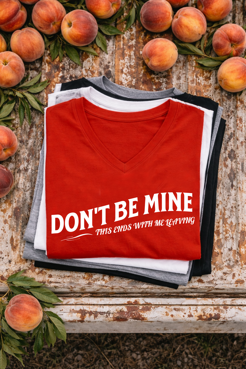 Red V-neck t-shirt with 'Don't Be Mine' text on a rustic wooden background with peaches.