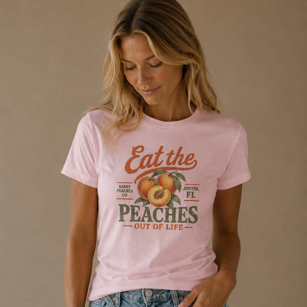 A woman wearing a light pink graphic t-shirt with a retro peach design and text, paired with light-wash blue jeans, standing against a solid beige studio background.