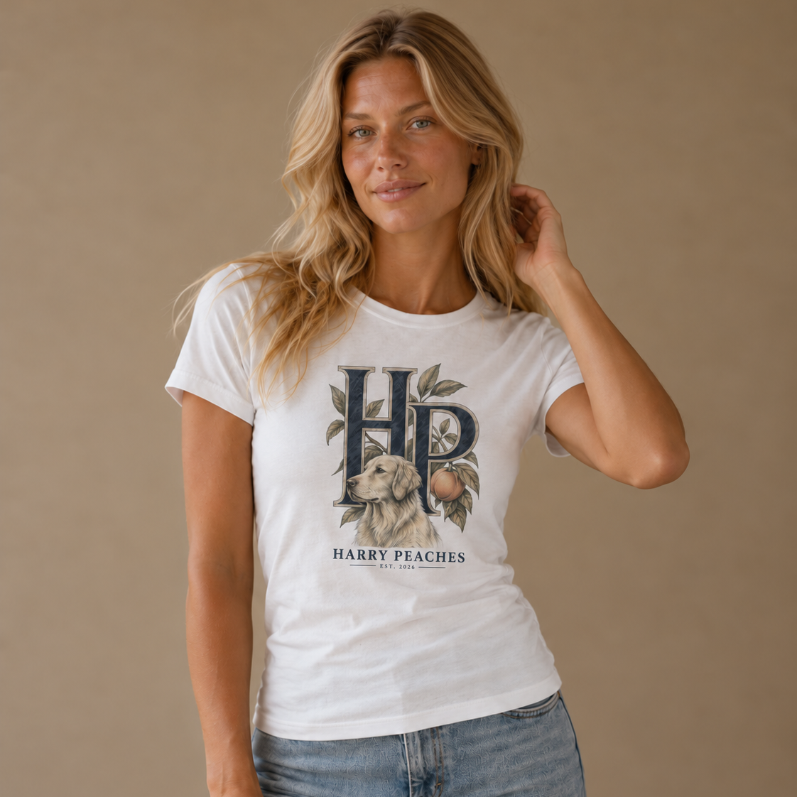 A woman modeling a white graphic t-shirt with a vintage-style 'HP' monogram and 'HARRY PEACHES' text over a peach illustration, paired with light-wash blue jeans against a solid beige studio background.