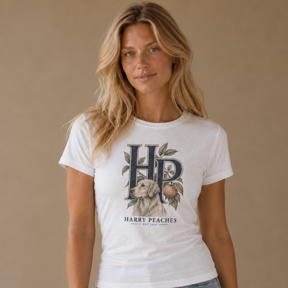 A woman modeling a white graphic t-shirt with a 'HP' monogram and 'HARRY PEACHES' text featuring a peach and dog illustration, paired with light-wash blue jeans against a solid beige studio background.