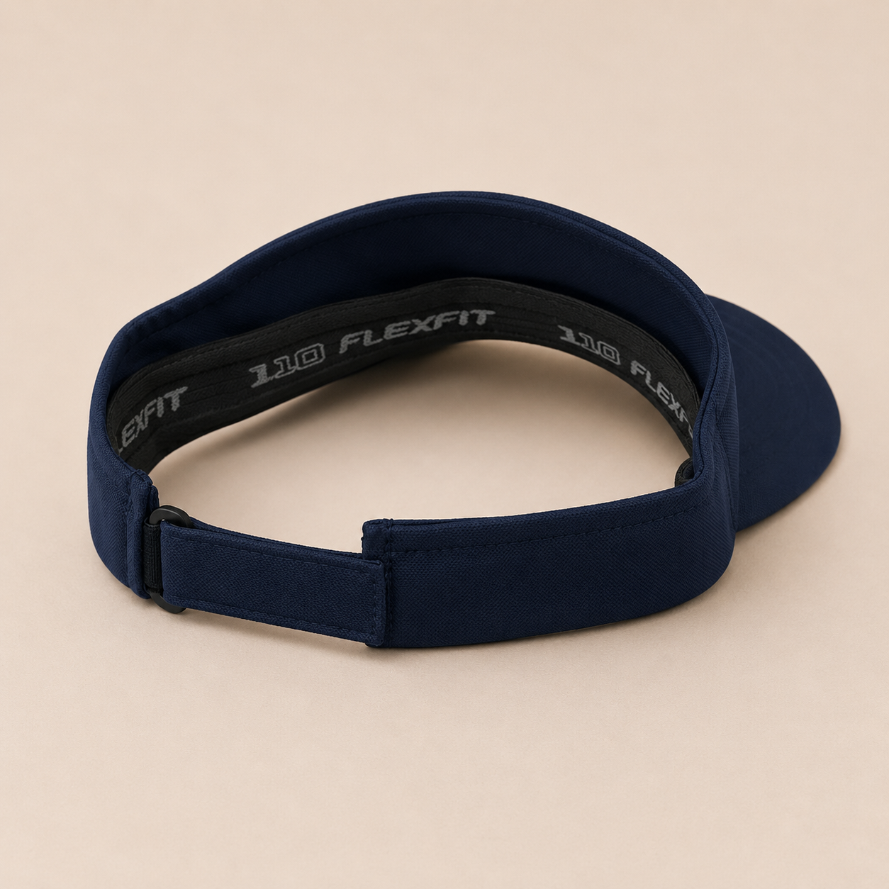 A navy blue athletic visor with an adjustable strap, featuring the '110 FLEXFIT' logo printed in white on the black inner band, set against a solid beige background.