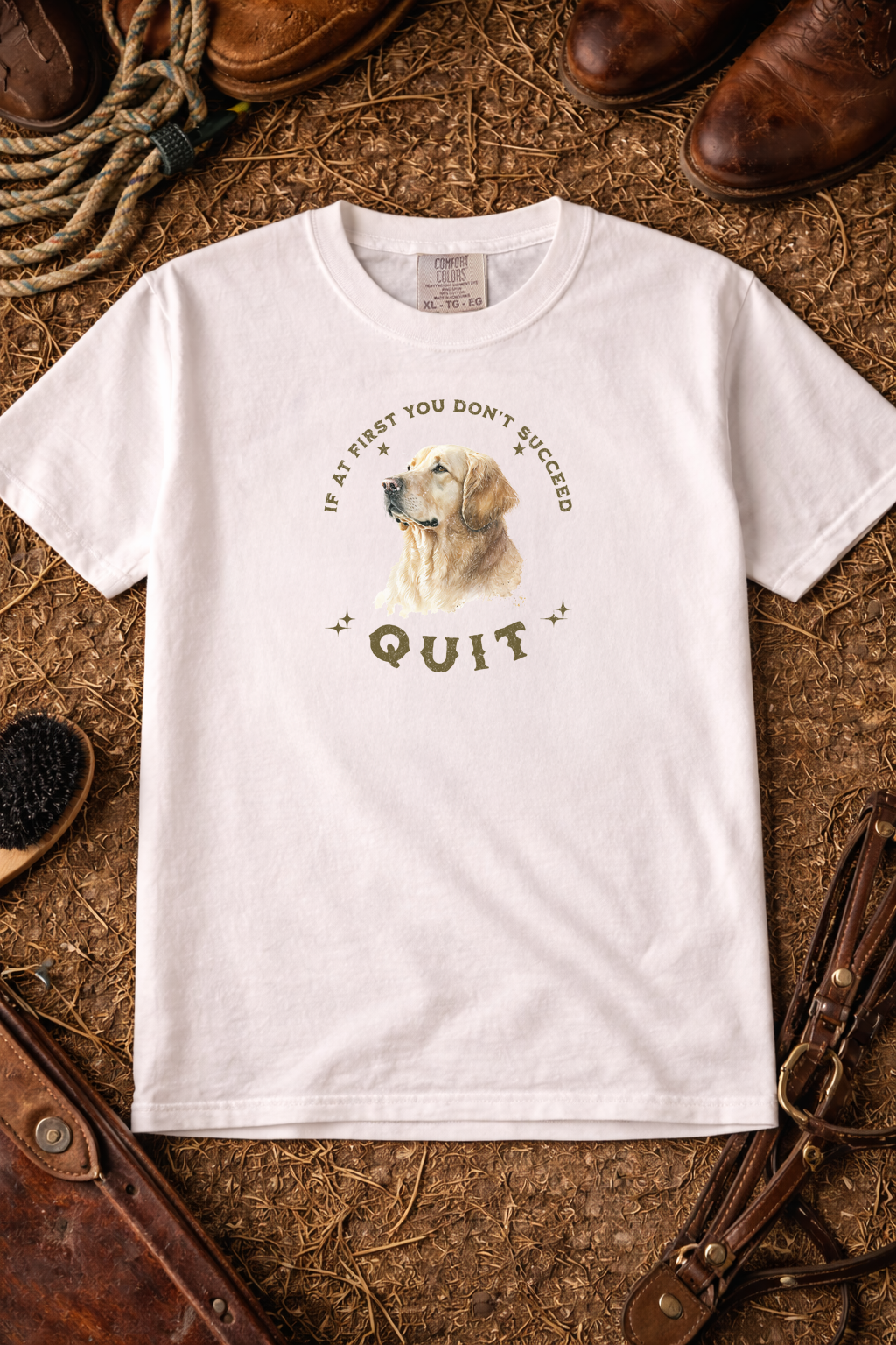 White t-shirt with a dog graphic and text on a rustic background with boots and leather items. If At First You Don't Succeed, Quit Graphic Tee