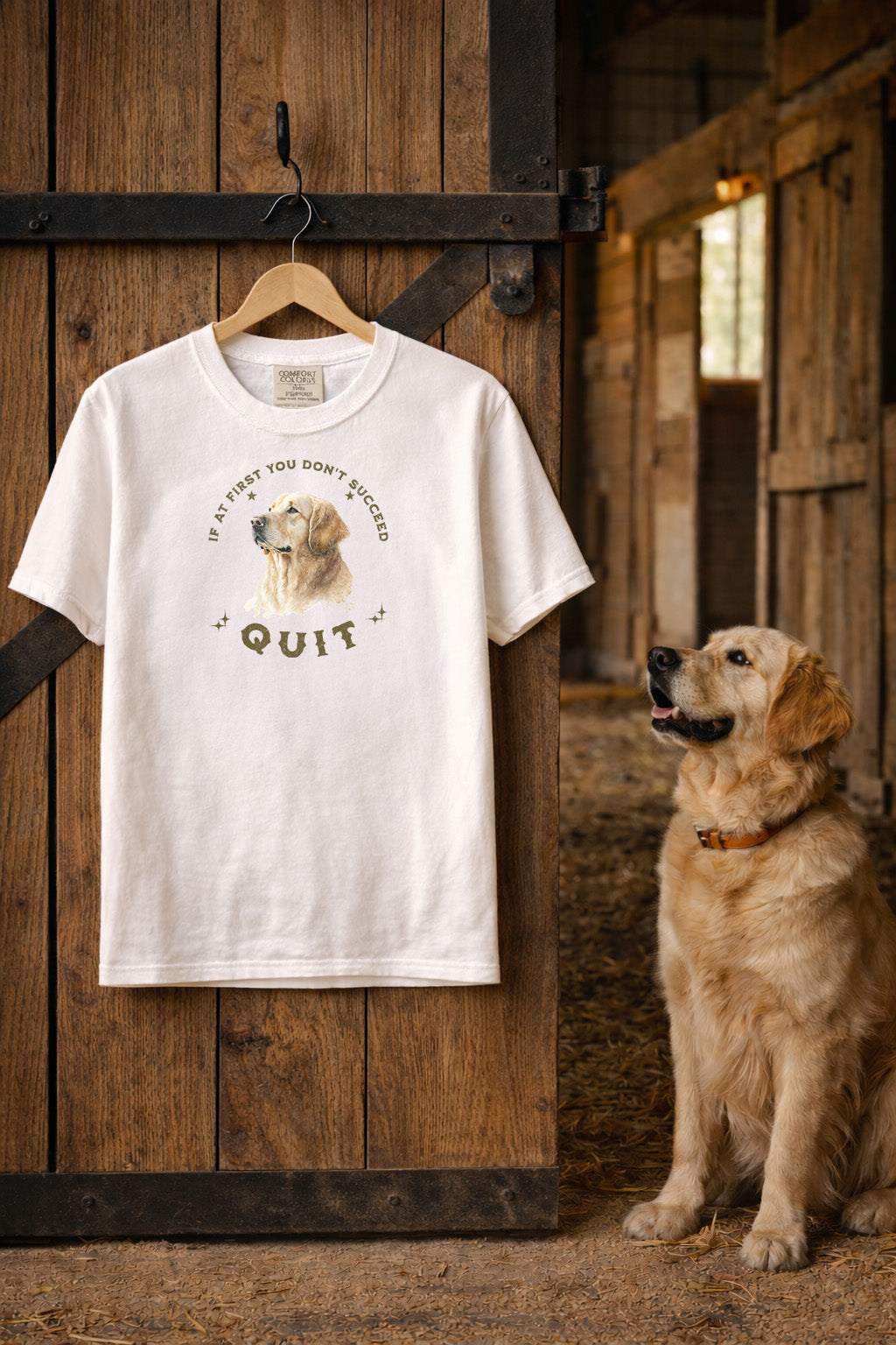 White t-shirt with a dog graphic and text on a hanger next to a golden retriever in a barn. If At First You Don't Succeed, Quit Graphic Tee