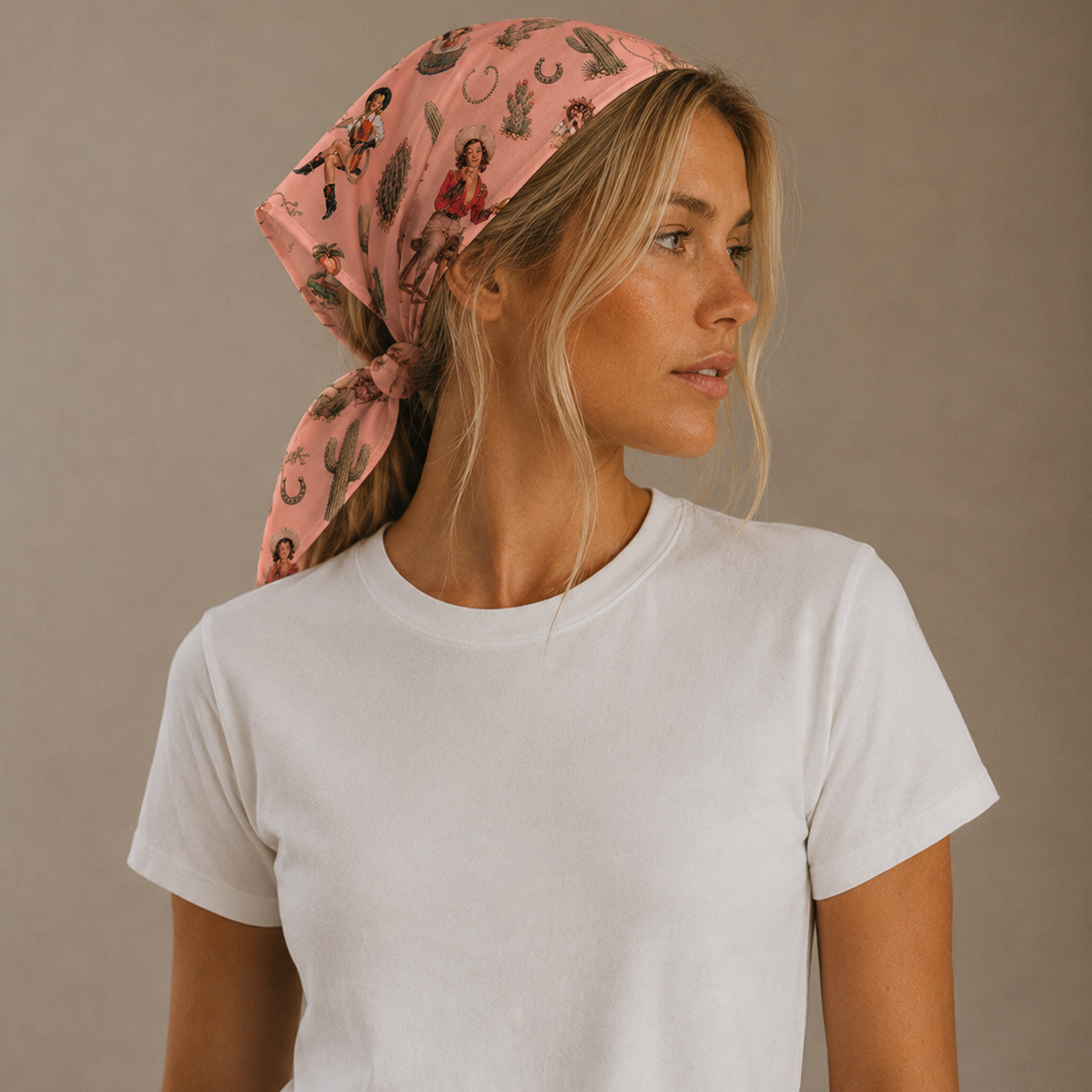 A woman wearing a light pink patterned headscarf and a plain white t-shirt, photographed against a neutral warm gray studio background.