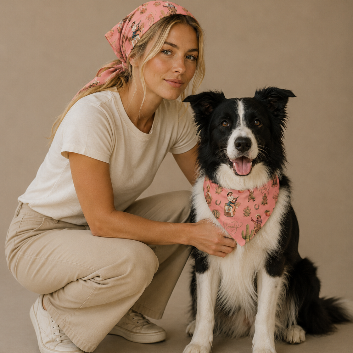 A woman crouches beside a black-and-white dog against a plain beige studio background. The woman wears a light pink patterned headscarf and white outfit, and the dog wears a matching pink patterned bandana.