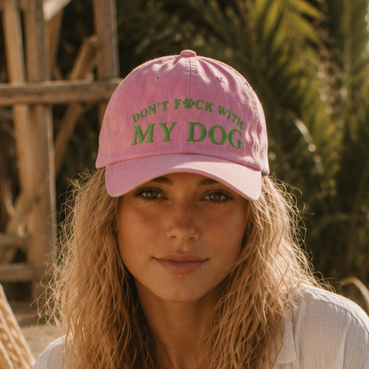 Woman wearing a pink cap with text, sitting with a dog outdoors.