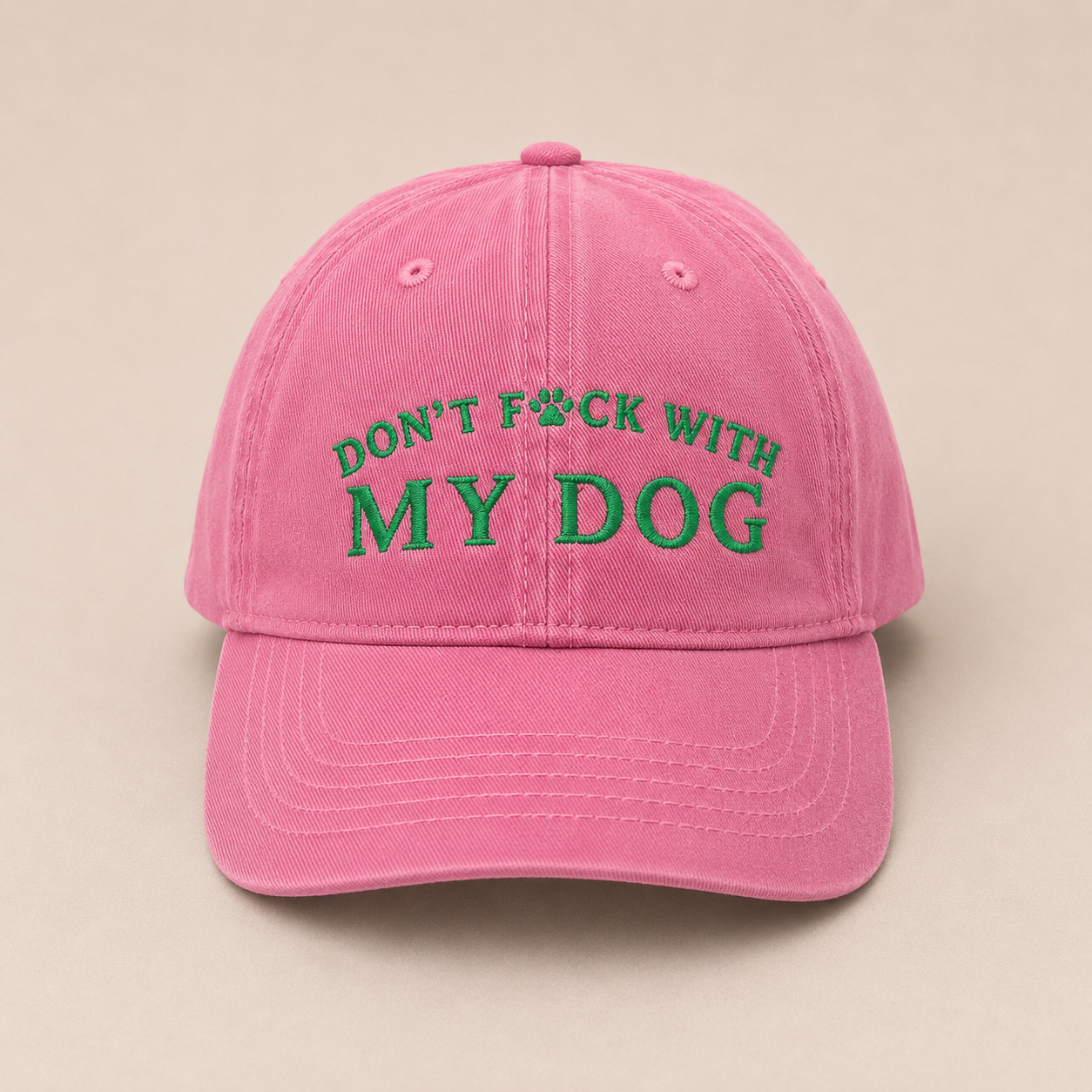 A pink baseball cap with green embroidered text reading 'DON'T F*CK WITH MY DOG' on the front, shown against a plain beige background.
