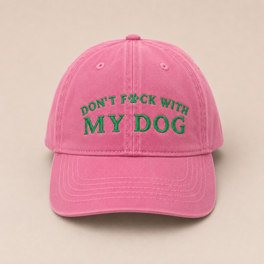 A pink baseball cap with green embroidered text reading 'DON'T F*CK WITH MY DOG' on the front, shown against a plain beige background.