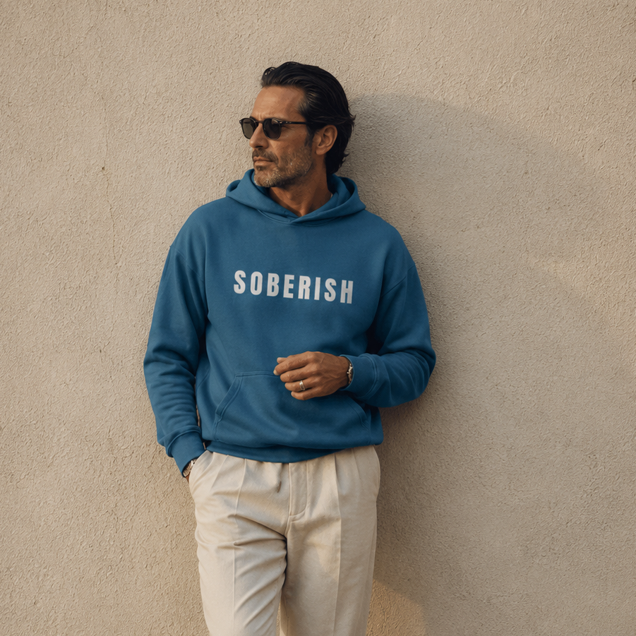 Man wearing a blue 'SOBERISH' hoodie against a beige wall.
