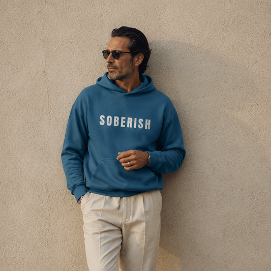 Man wearing a blue 'SOBERISH' hoodie against a beige wall.