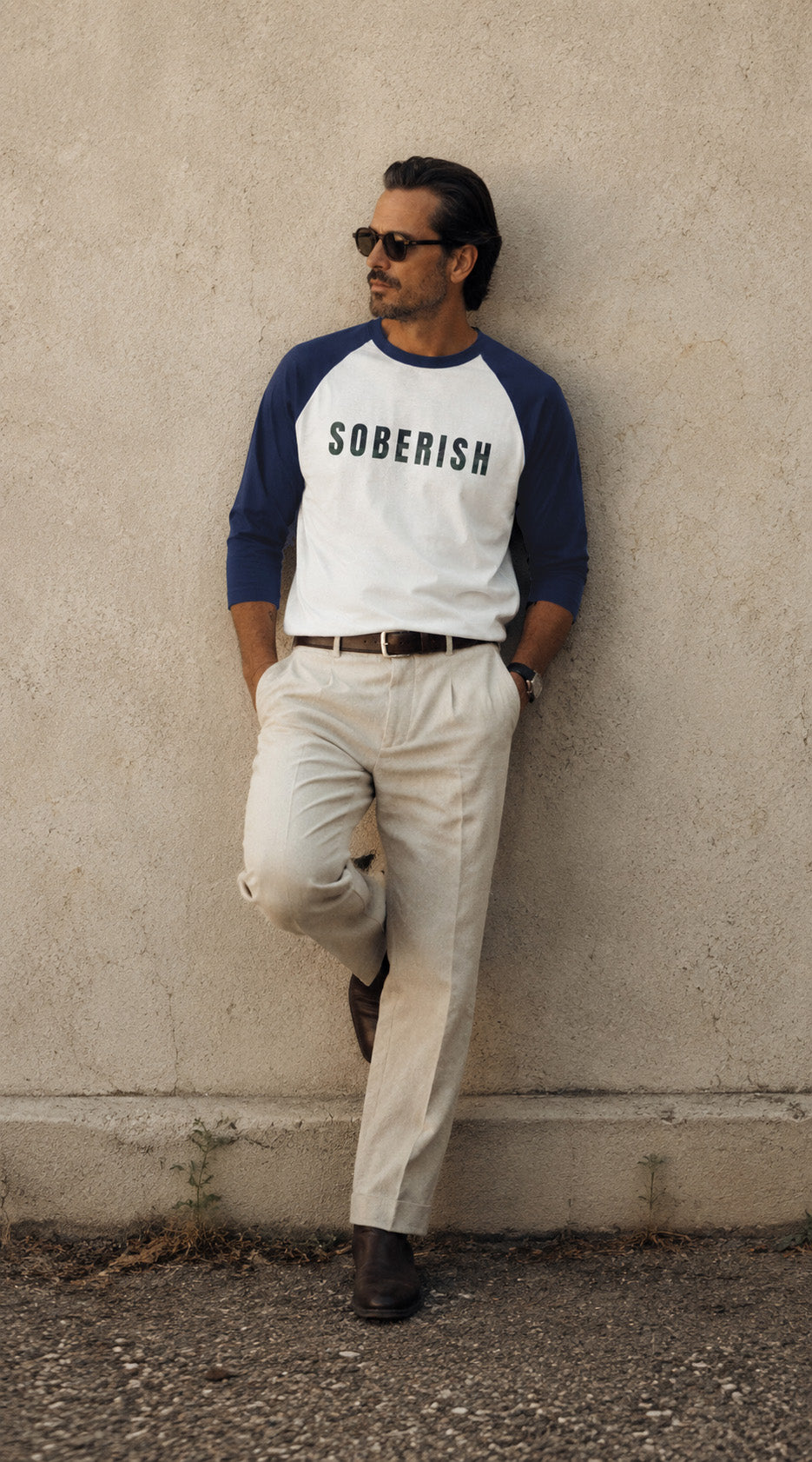 Man wearing a 'SOBERISH' baseball shirt leaning against a wall.