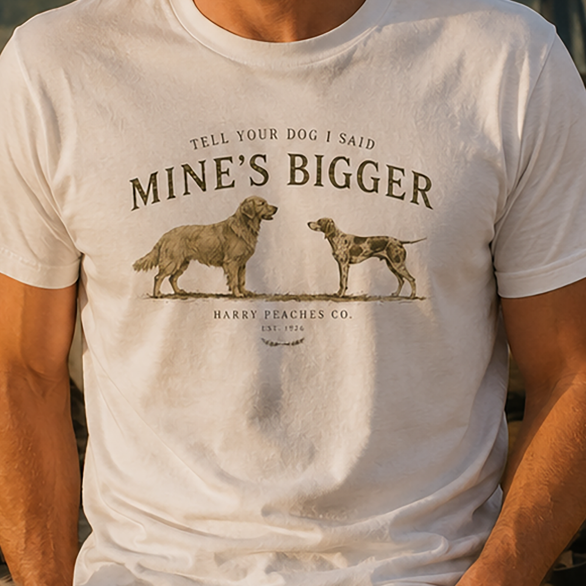 White t-shirt with graphic of two dogs and text 'Tell your dog I said mine's bigger' by Harry Peaches Co.