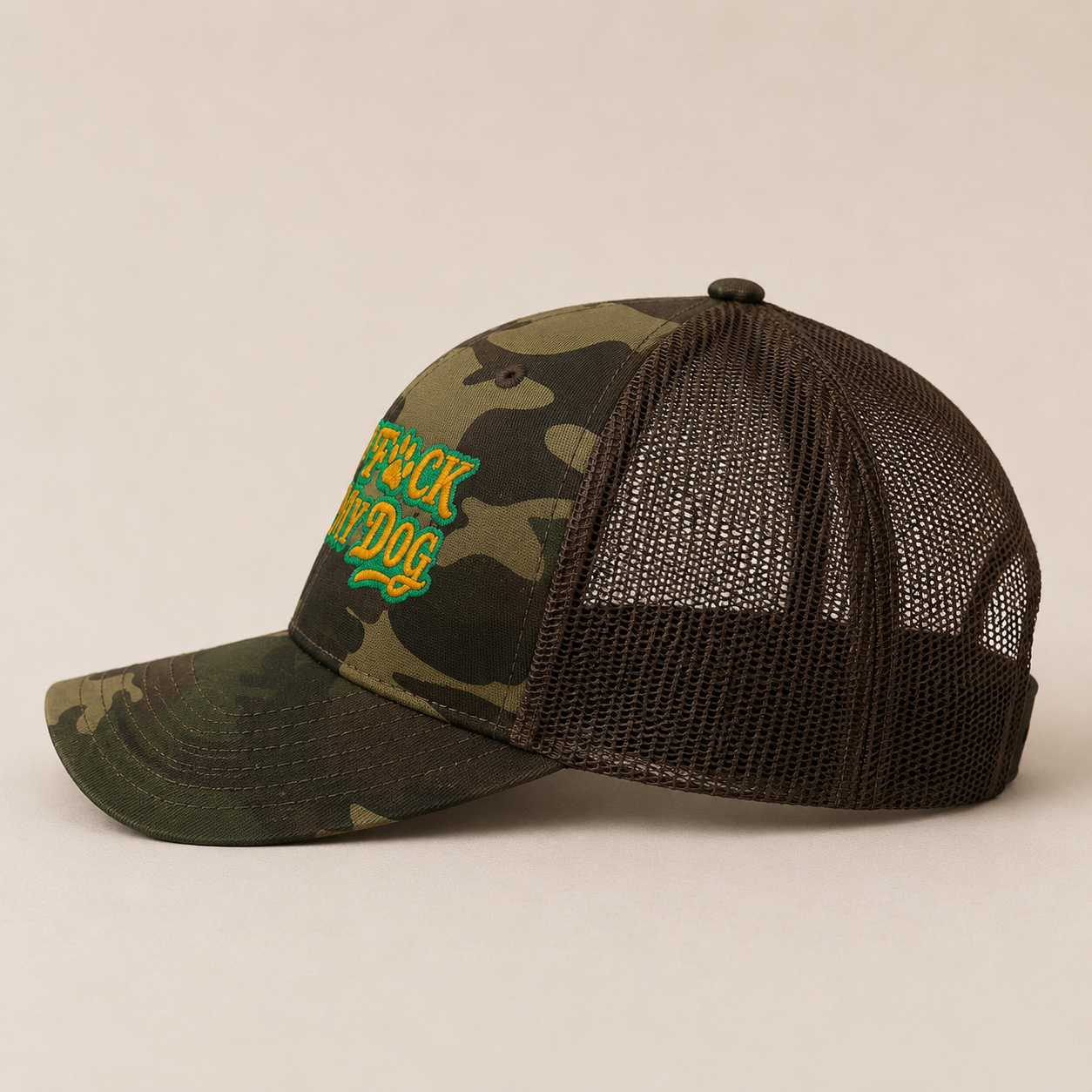 A camouflage trucker hat with a dark brown mesh back and a green and yellow embroidered patch on the front that reads 'BACK DOG'.