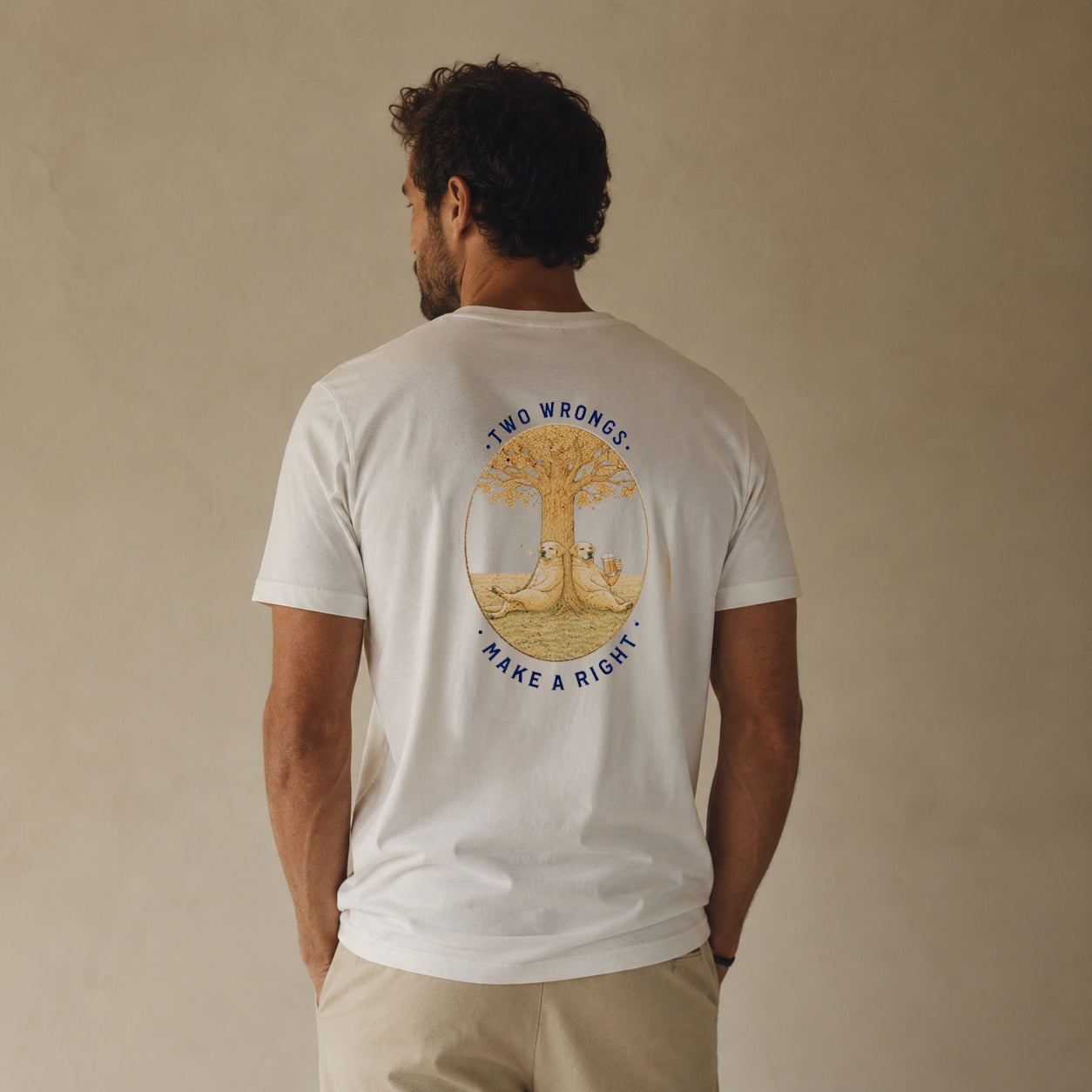 A man viewed from behind wearing a white t-shirt with a large graphic on the back. The graphic features a golden tree with two rabbits sitting under its branches, surrounded by the text 'TWO WRONGS, MAKE A RIGHT'.